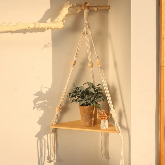 Rustic wooden wall shelf with macrame hanging, used as a plant stand in a cozy boho living room corner.
